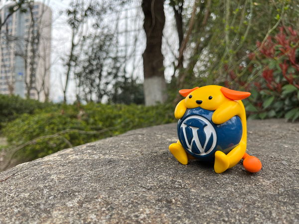 toy Wapuu, the WordPress mascot, sitting on a rock with trees and tall skyscrapers in the background